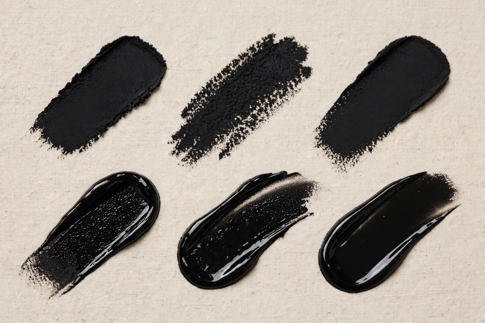 Black eyeliner swatches in matte and glossy finishes on a beige surface